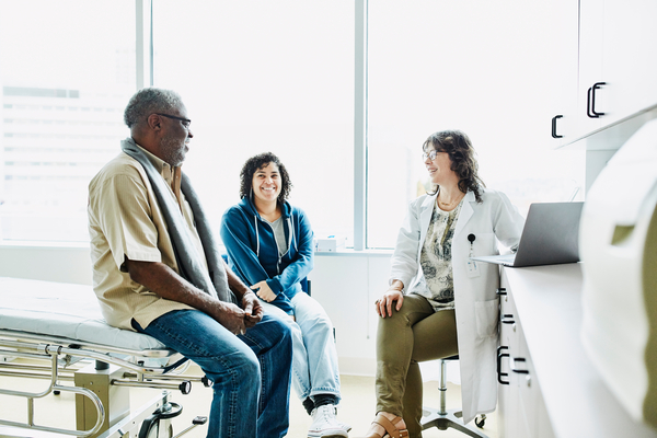 Smiling female doctor consulting with senior male patient and adult daughter in exam room